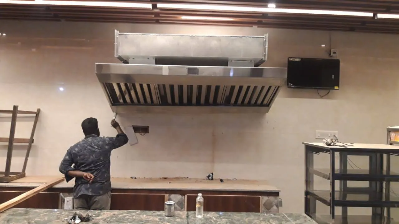 Technician fitting a stainless steel exhaust hood in a commercial kitchen